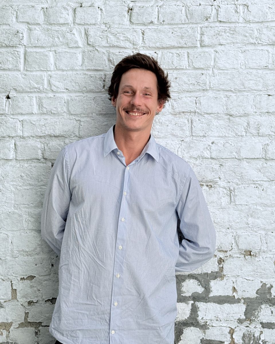 Max Wouters, fondateur de SansAdmin, souriant devant un mur de briques blanches